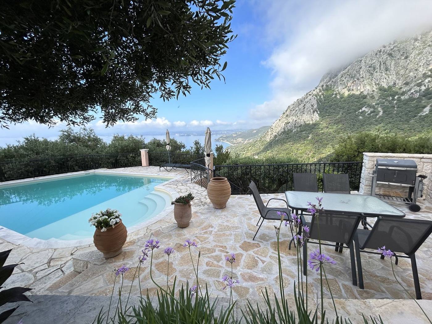 Pool and terrace table under the olive tree, with the slopes of Pantokrator