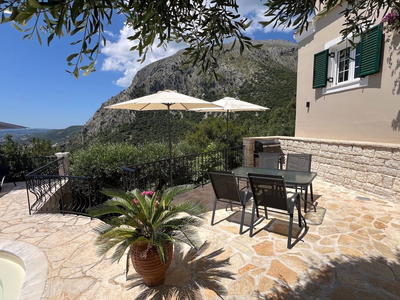 Side terrace with a table, green shutters and the mountain