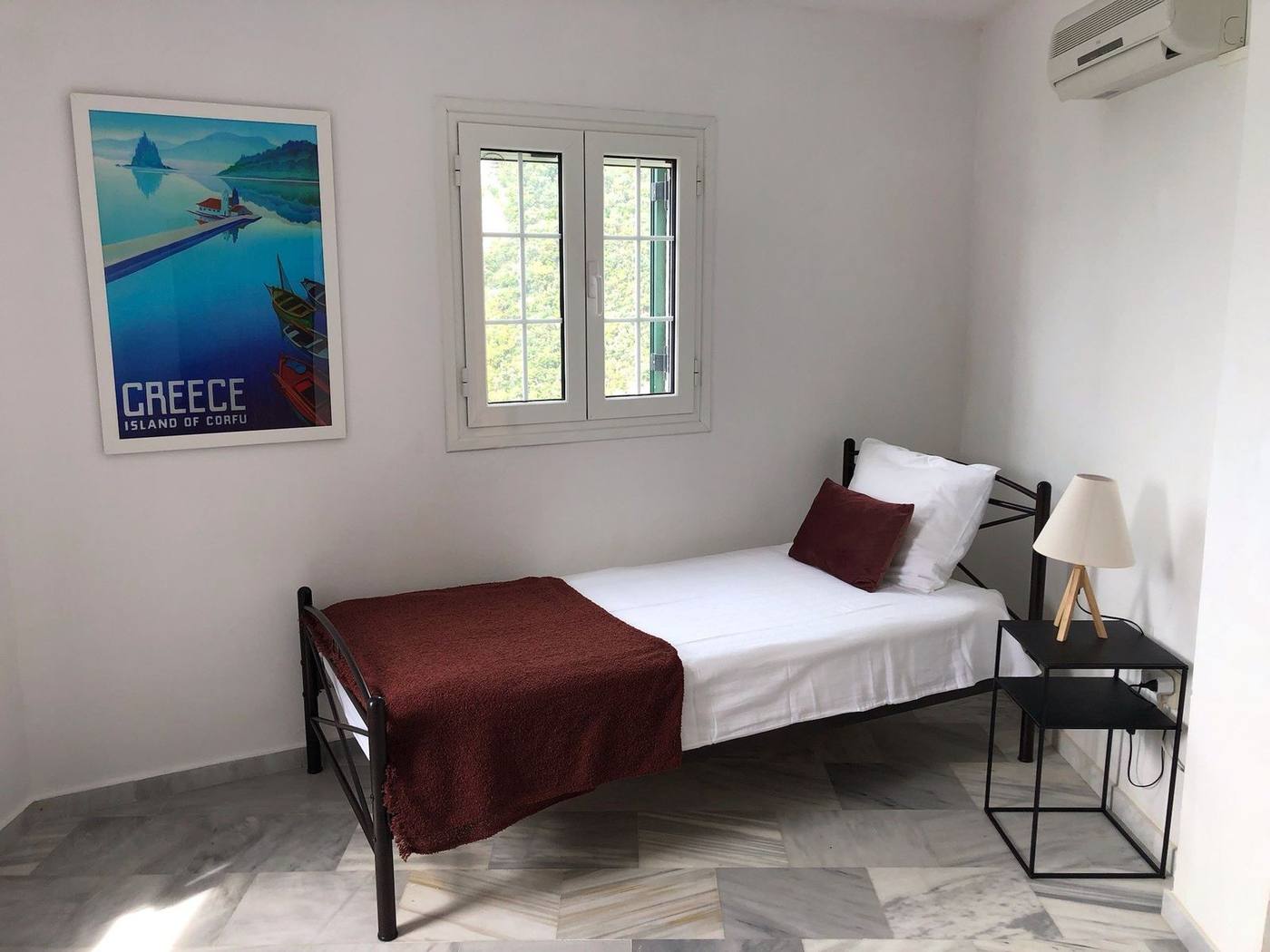 Single bed beneath a Greece travel poster
